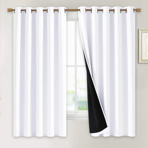 White blackout curtains with bronze grommet tops hanging on a window. One panel reveals black thermal lining.