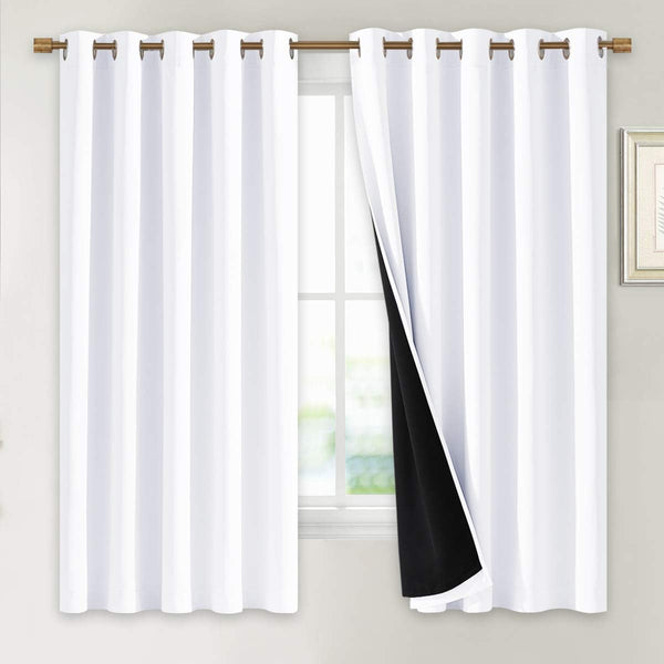 White blackout curtains with bronze grommet tops hanging on a window. One panel reveals black thermal lining.