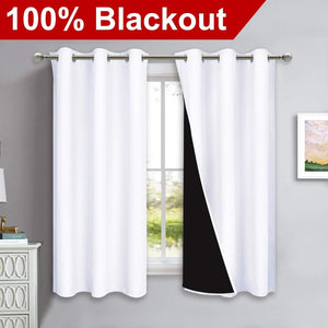 Two white blackout curtains with silver grommet tops hanging on a rod, one pulled back revealing black lining.