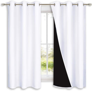 Pair of white blackout curtains with visible black lining and silver grommet tops on a window rod.