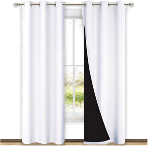 Pair of white blackout curtains with silver grommet tops hanging on a window rod, revealing a black thermal lining.