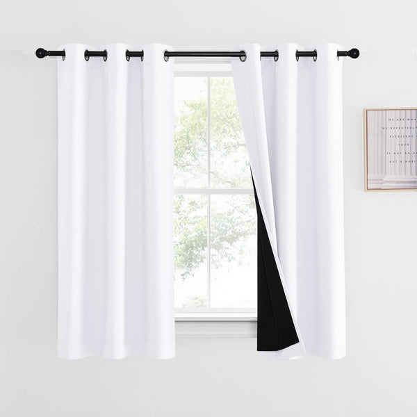 White blackout curtains with black lining and grommet top, hanging on a black rod.