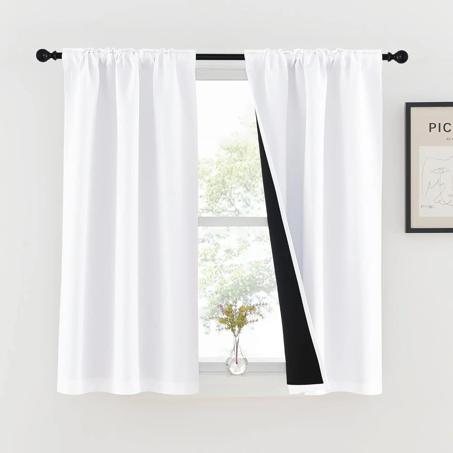 White rod pocket blackout curtains on a black curtain rod in a bright modern room