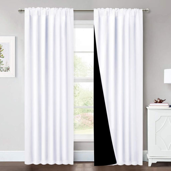 White rod pocket blackout curtains hanging on a window. One panel pulled back shows its dark lining.