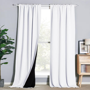 White rod pocket blackout curtains hanging on a window, one panel revealing its black backing.