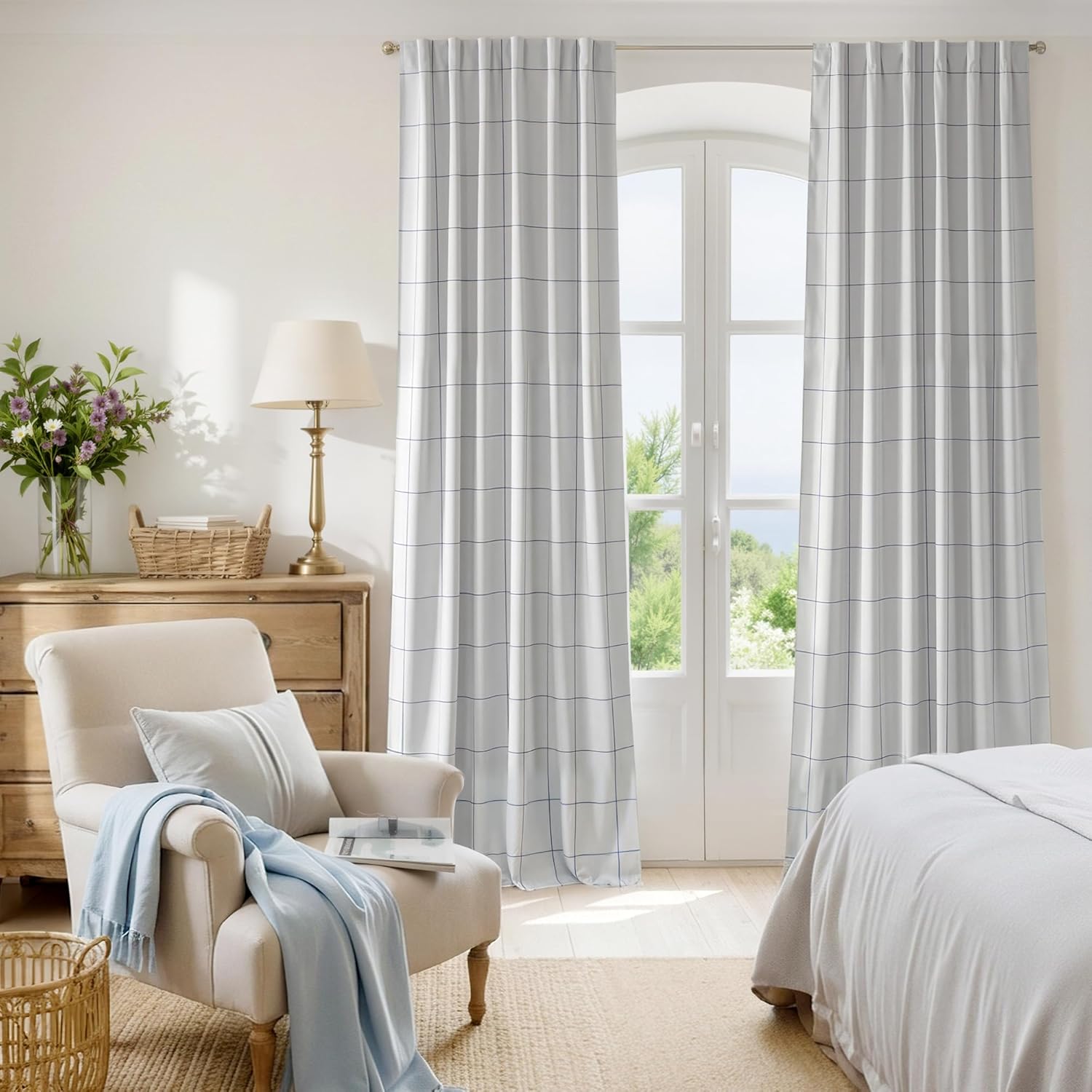 White curtains with a subtle blue grid pattern and pleated top hanging on a bedroom window.