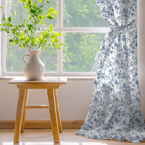 White curtain with blue floral rose pattern and ruffled bottom edge, tied back from a sunlit window.