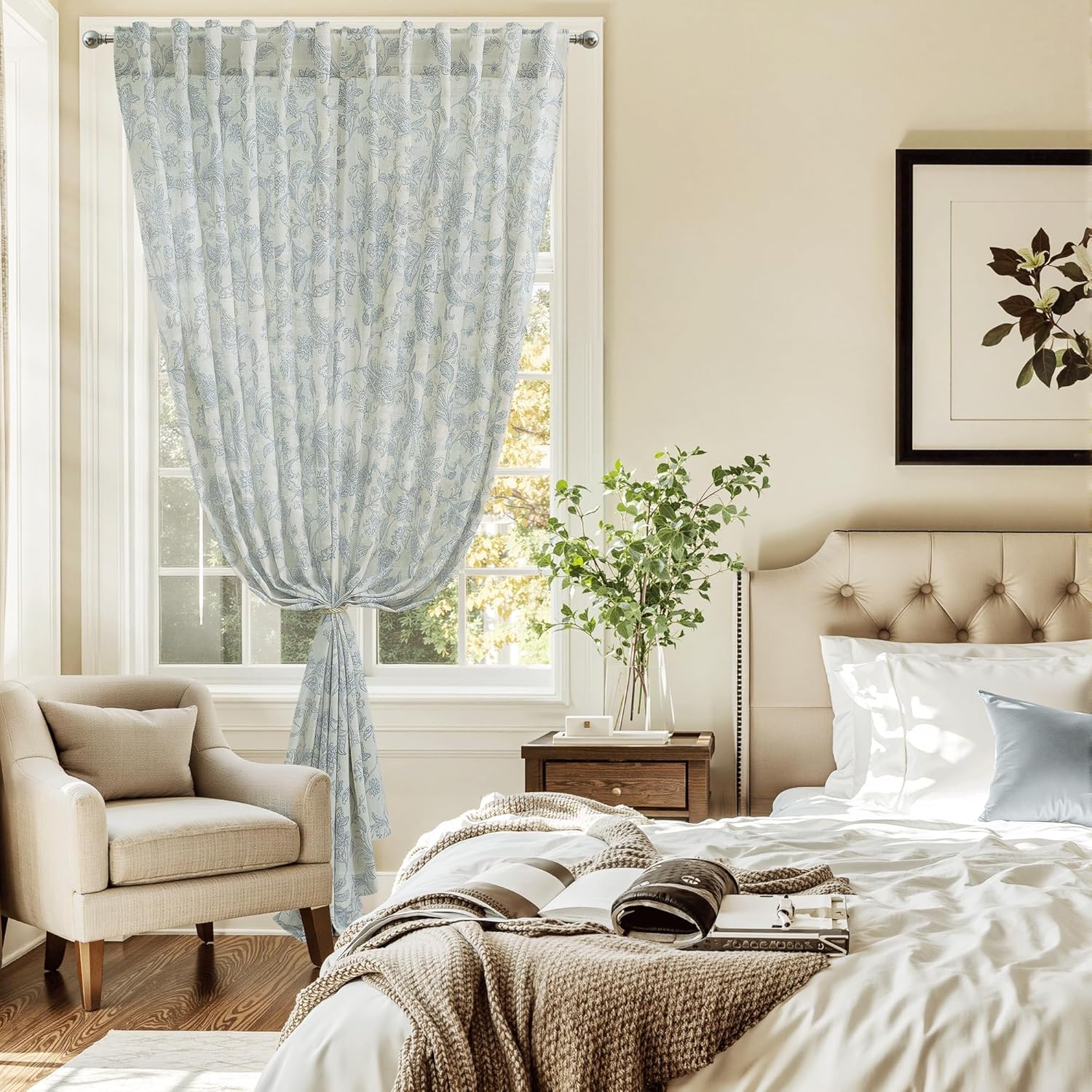 White sheer window curtain with light blue floral pattern, grommet top, tied back in a sunny bedroom.