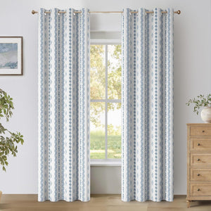 Two white curtain panels with blue geometric vertical patterns and grommet tops hanging in a bright room.