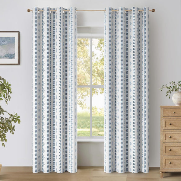Two white curtain panels with blue geometric vertical patterns and grommet tops hanging in a bright room.