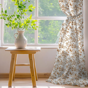 White curtain panel with a brown vintage rose floral pattern, tied back by a sunlit window.