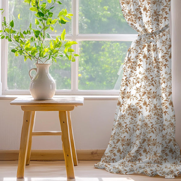 White curtain panel with a brown vintage rose floral pattern, tied back by a sunlit window.