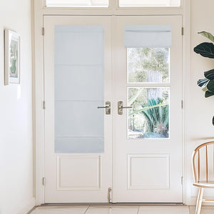 White cordless Roman blackout shades installed on glass French doors; one lowered, another raised, providing light and privacy control.
