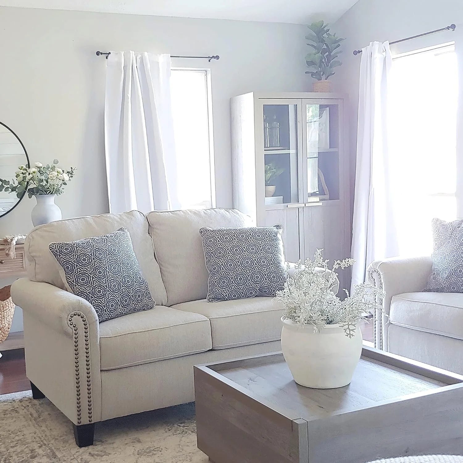 White curtains framing bright windows in a neutral living room with beige sofa