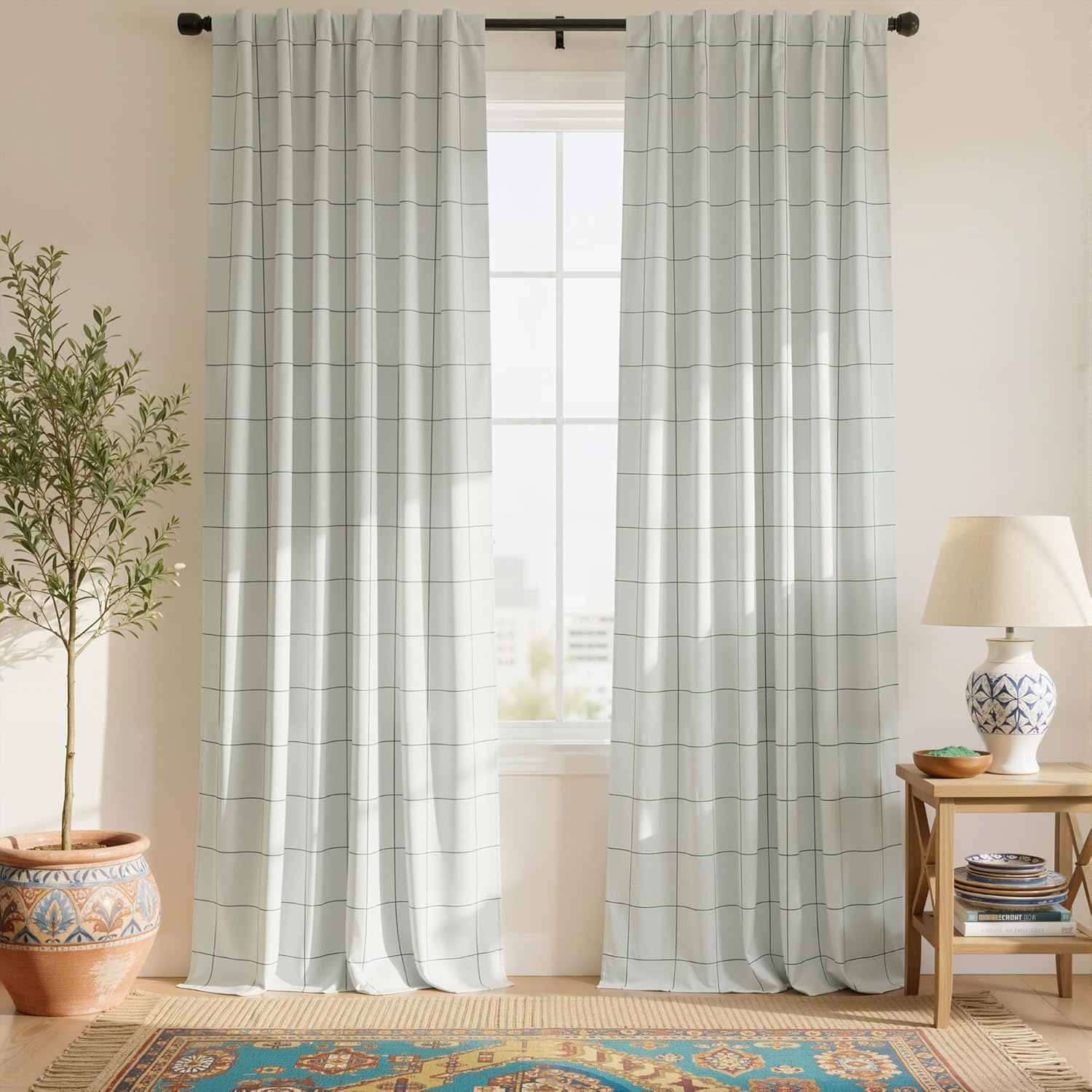 Pair of white fabric curtains featuring a dark grid pattern, hung on a black rod in a sunlit room.