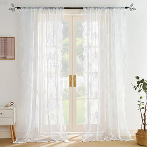White embroidered sheer curtains with scalloped lace edges, hanging on a rod over glass doors.