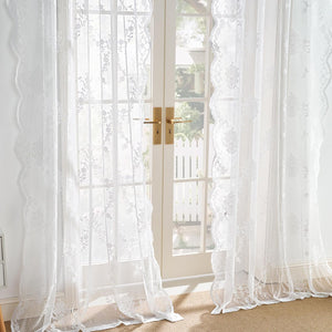 White floral lace sheer curtains with scalloped edges hanging on french doors, letting in soft light.