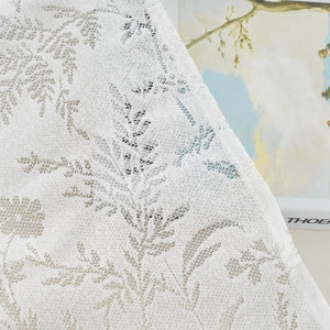 Close-up of a delicate white sheer lace curtain panel featuring an intricate floral and leaf pattern.