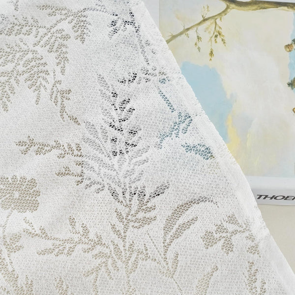 Close-up of a delicate white sheer lace curtain panel featuring an intricate floral and leaf pattern.
