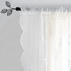 White sheer lace curtain with delicate floral pattern and scalloped edge, hanging on a decorative black leaf finial rod.