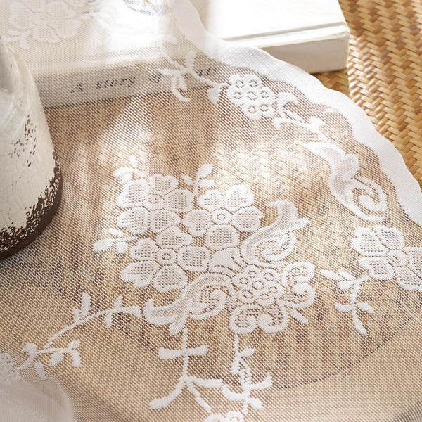White floral lace table runner with delicate flower patterns, sheer mesh, and scalloped edge.
