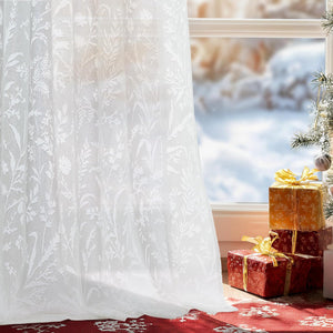 White sheer lace curtain with a delicate botanical pattern, softly filtering light by a winter window.