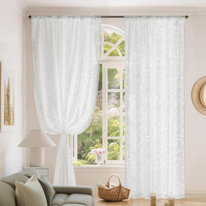 White sheer rod pocket curtains with delicate floral embroidery. One panel tied back revealing a bright garden.
