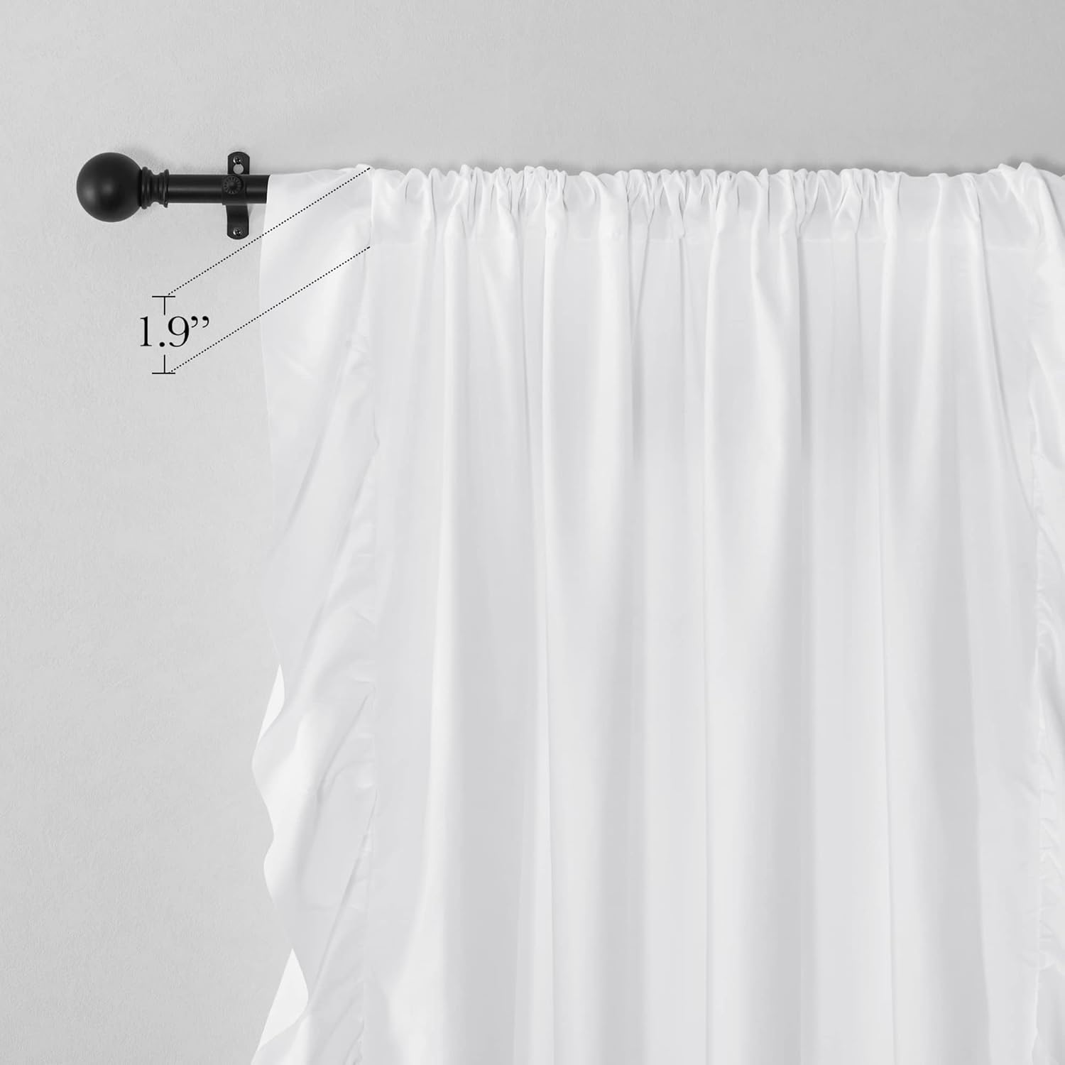White fabric curtain with gathered top hanging on a black metal rod with a ball finial.