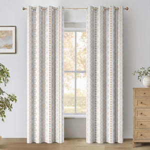 Pair of white curtains with rustic geometric patterns and brass grommet tops, hanging in a bright window.