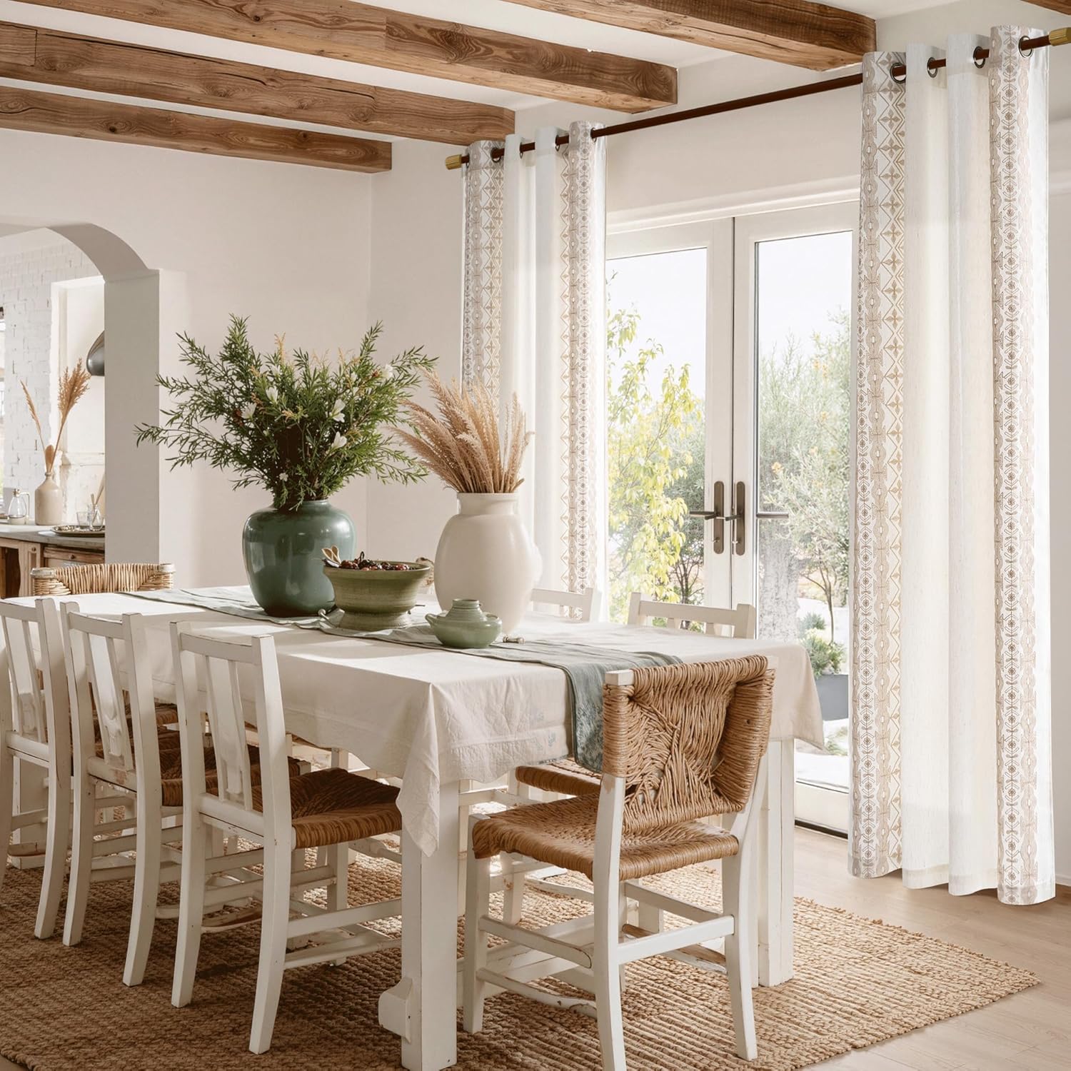 White sheer curtains with tan geometric border, grommet top, framing bright doors in a dining room.