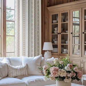 White fabric curtains with vertical stripes of gold geometric and floral patterns in a rustic room.
