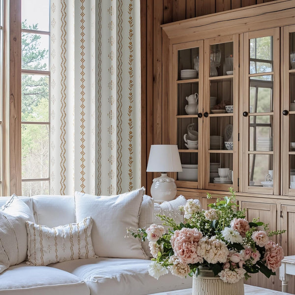 White fabric curtains with vertical stripes of gold geometric and floral patterns in a rustic room.