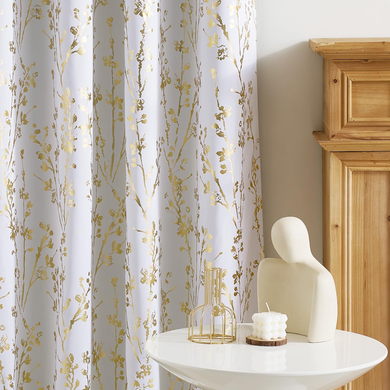 Elegant white curtain with shimmering gold botanical branch pattern, hanging in a bright room.