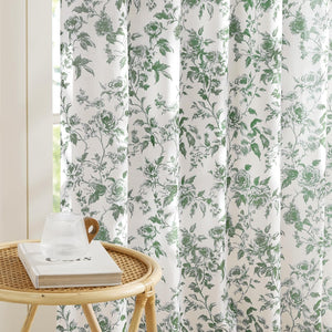 White curtains with an intricate green vintage rose floral pattern hanging gracefully by a window.