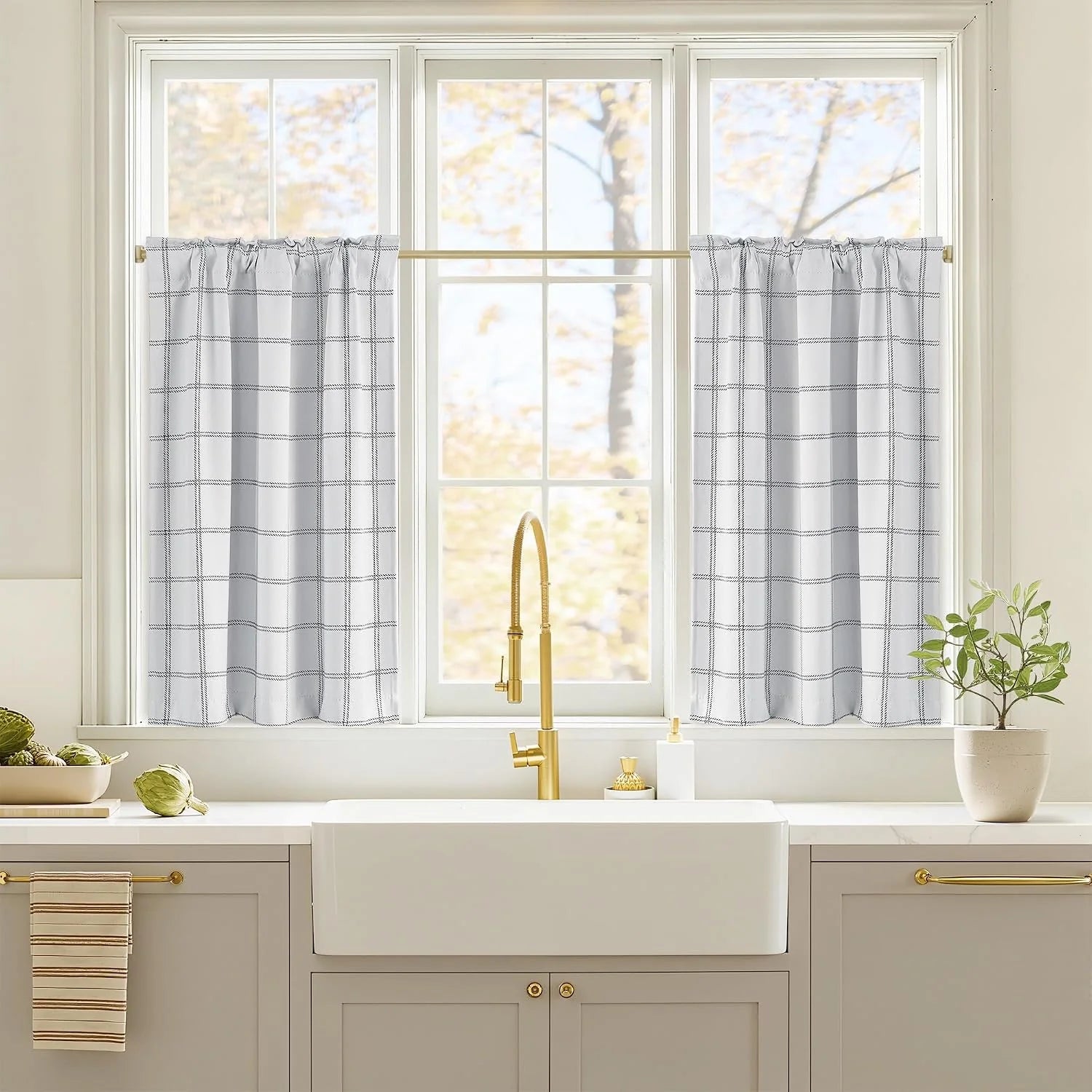 White grid-pattern cafe curtains on brass rod above a farmhouse kitchen sink