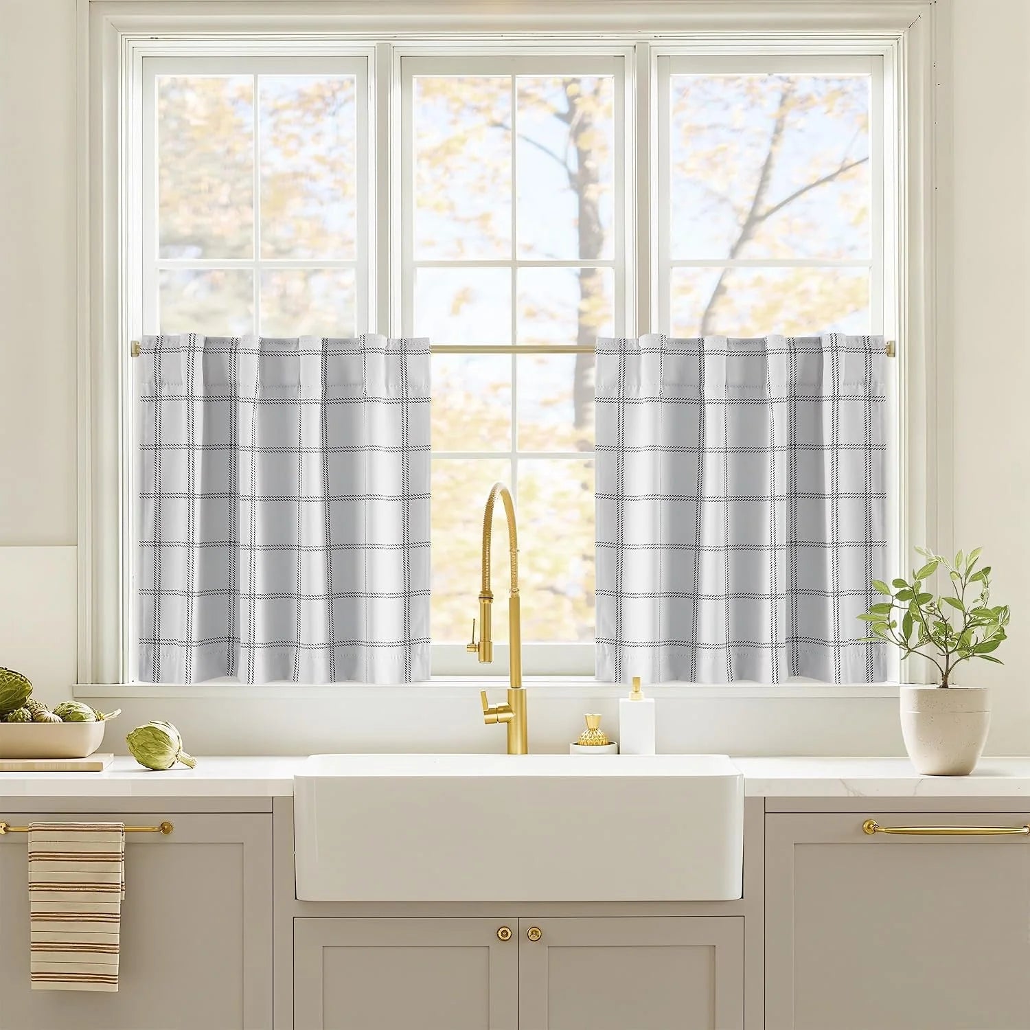 White grid-pattern cafe curtains on a brass rod above a farmhouse kitchen sink