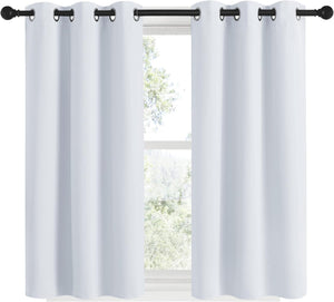 Pair of crisp white blackout curtains with dark grommets hanging on a black curtain rod in front of a window.