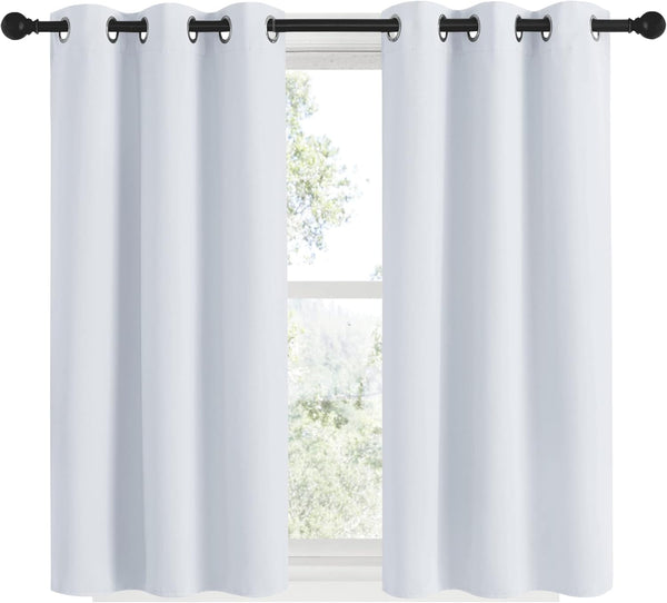 Pair of crisp white blackout curtains with dark grommets hanging on a black curtain rod in front of a window.