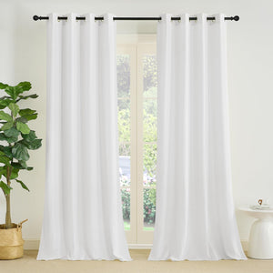Pair of white blackout curtains with black grommet tops, hanging on a black rod in a bright room.