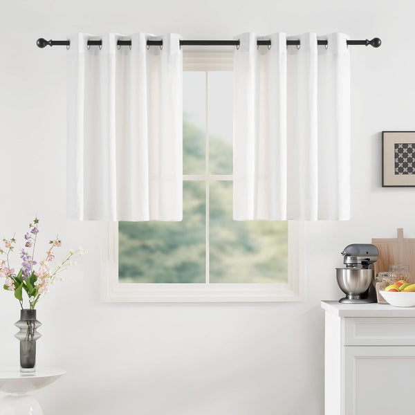 White grommet tier curtains on black rod in a bright kitchen window. Mixer and flowers visible.