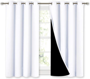 White blackout curtains with silver grommet tops. Right panel slightly pulled back reveals black thermal lining.