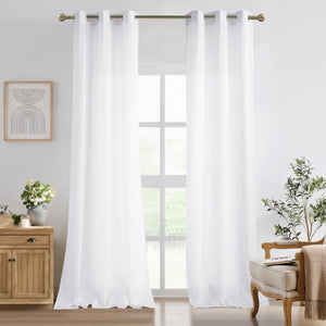 Two panels of solid white grommet top curtains hanging on a bronze rod in a bright living room.
