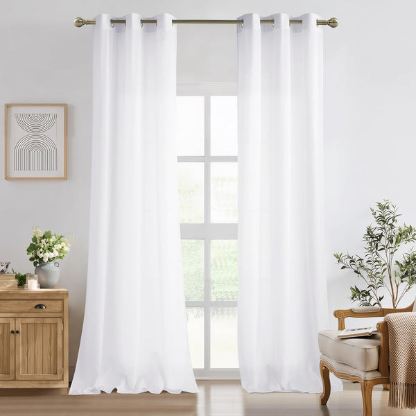Two panels of solid white grommet top curtains hanging on a bronze rod in a bright living room.