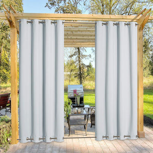 Two panels of white grommet top outdoor curtains hanging on a wooden pergola, showing a patio.