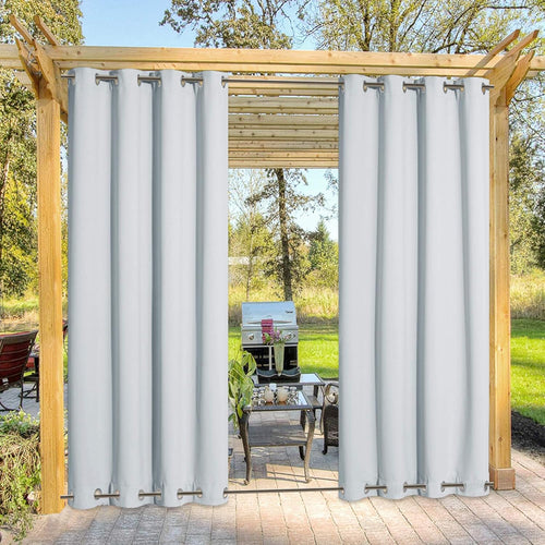 Two panels of white grommet top outdoor curtains hanging on a wooden pergola, showing a patio.
