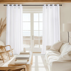 White grommet top curtains on a black rod, filtering light in a bright living room with an ocean view.