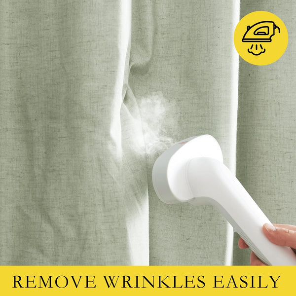 White handheld steamer emitting steam to smooth wrinkles from light sage green fabric.