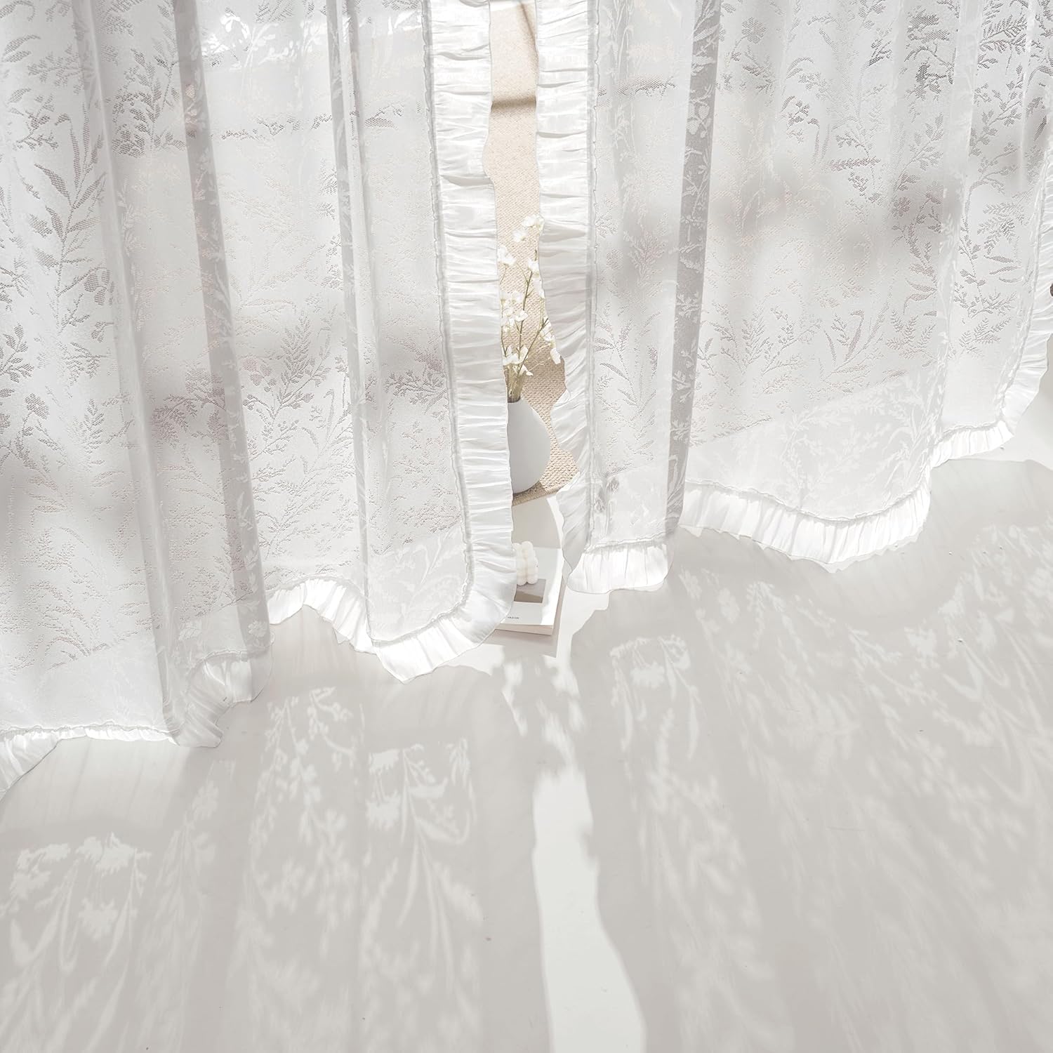 Elegant white sheer curtains with subtle floral jacquard pattern and ruffled edges, allowing diffused sunlight to enter.