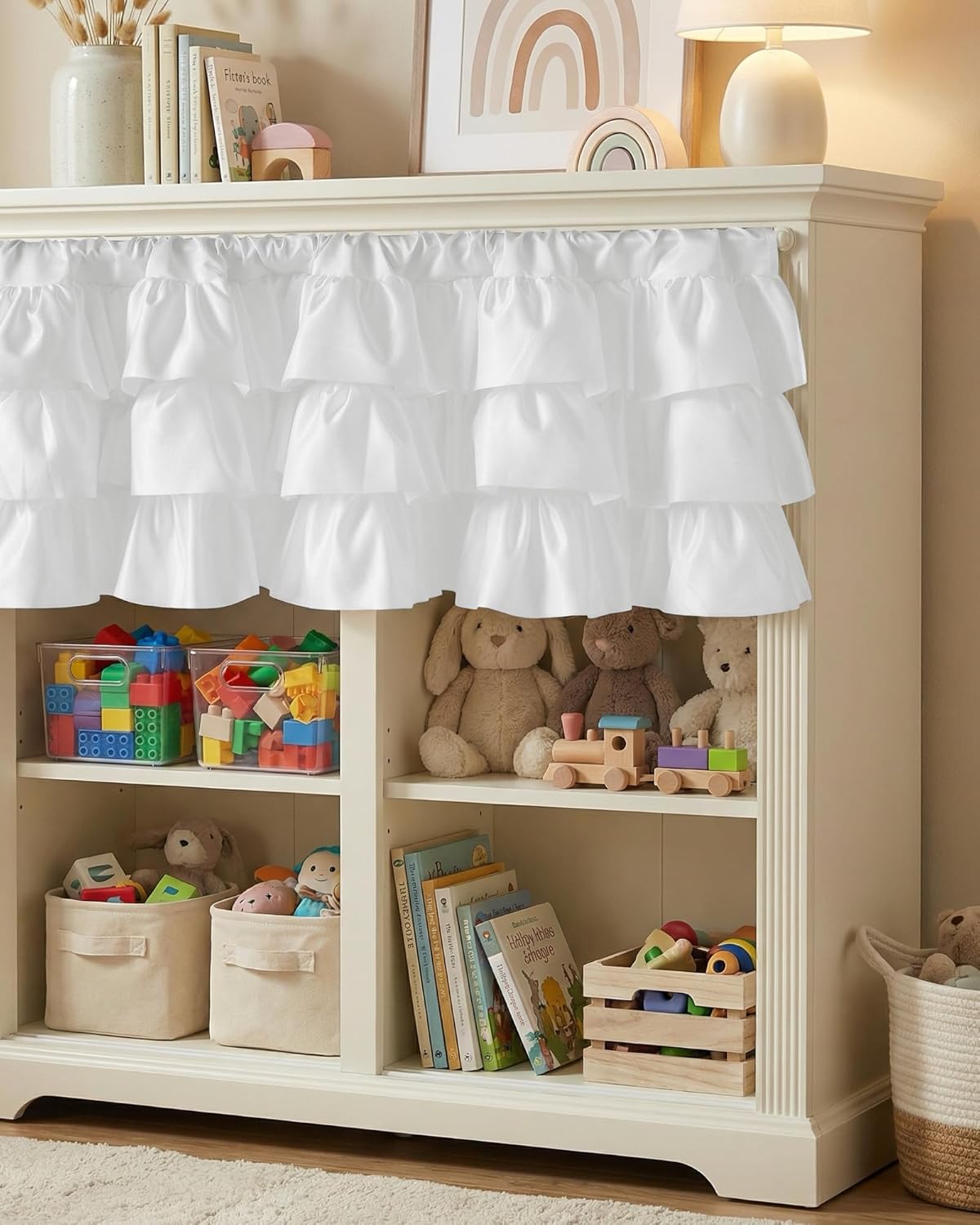 White layered ruffle valance covering the top shelves of a child's toy cabinet.