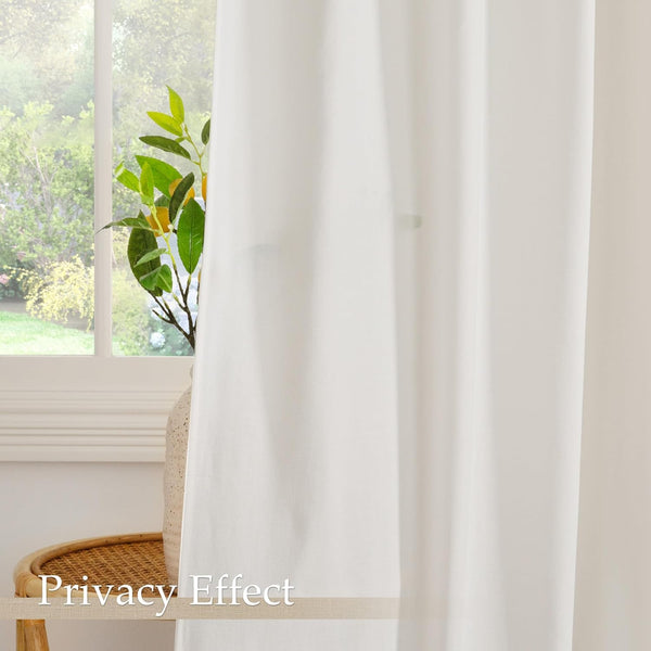 White linen-look privacy curtain hanging in front of a sunlit window, obscuring the view of a green plant.